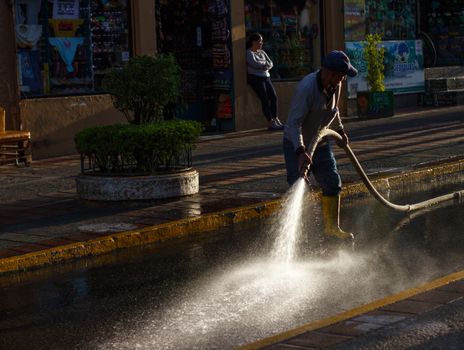 A city worker uses a hose to clean a street at dusk, highlighting urban maintenance.