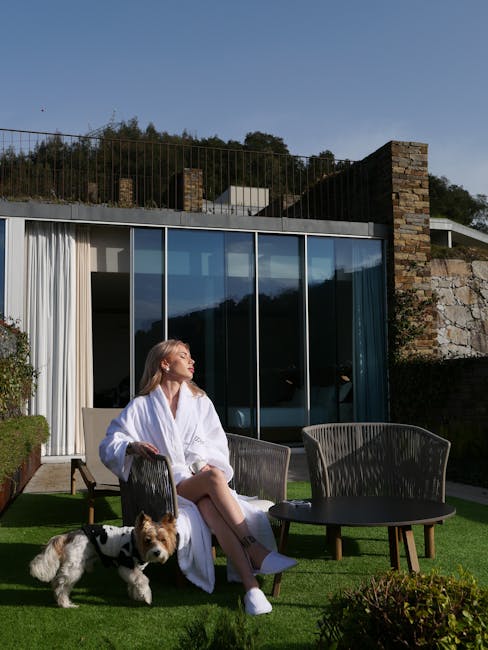 A woman in a robe enjoys the sun with her dog in a stylish outdoor garden.